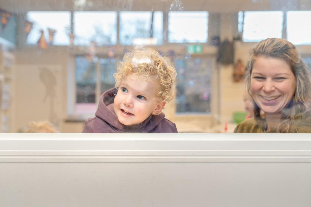 Jongen kijkt nieuwsgierig door het raam op de kinderopvang