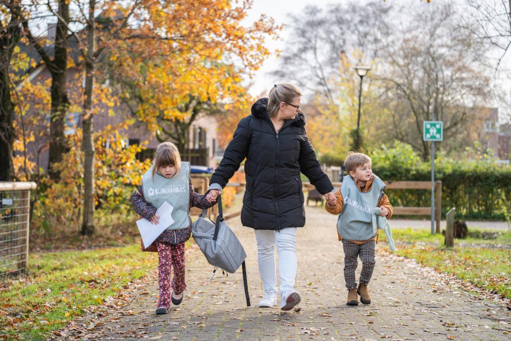 Pedagogisch medewerker loopt met twee kinderen aan de hand